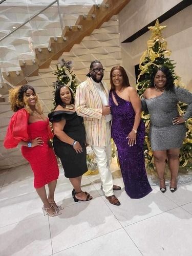 Five people pose in formal attire beside a decorated Christmas tree on a staircase landing.