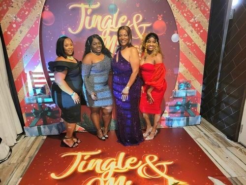 Four women posing in formal dresses on a red carpet in front of a “Jingle” holiday backdrop