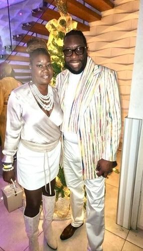 Two people posing indoors in white outfits, standing under warm lighting.