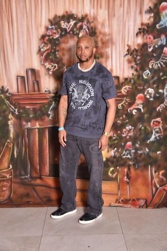 Man standing on a tiled floor before a painted floral backdrop and Christmas trees