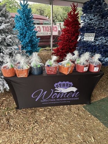 Display of colorful tinsel Christmas trees on a vendor table with a “Women” logo banner