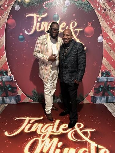 Two men posing on a festive red carpet before a “Jingle & Mingle” holiday backdrop