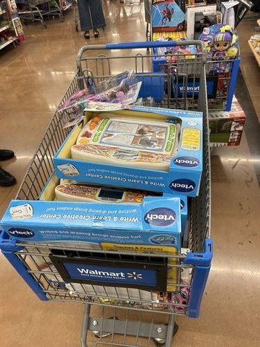Shopping cart filled with boxed toys in a store aisle
