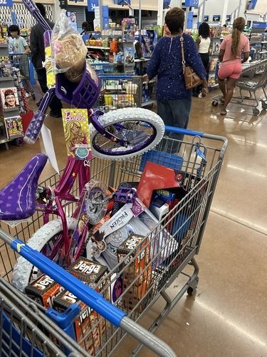 Shopping cart full of toys in a store aisle, with a purple child’s bicycle beside it.