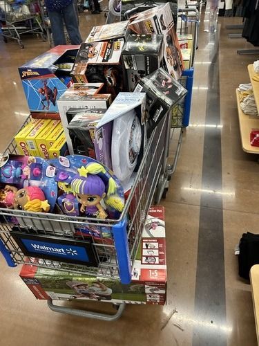 Shopping cart full of assorted toy boxes and stuffed animals in a store aisle