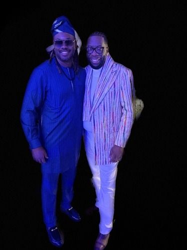 Two people posing together at a formal event, one in a blue outfit and one in a light striped suit.