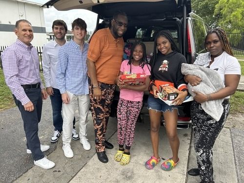Group posing beside an open vehicle, smiling while holding food boxes and bags of clothing