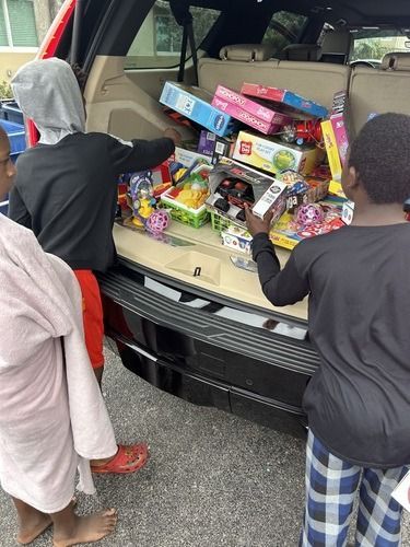 Children loading boxed toys into an open car trunk in a parking lot