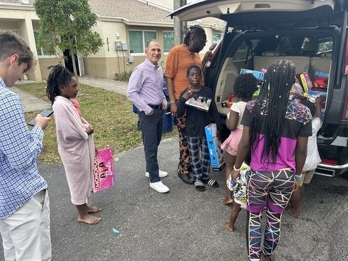 People unloading bags from an open SUV in a suburban driveway, preparing to leave or arrive.