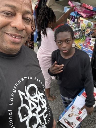 Man smiling beside a serious child at a market stall with toys and snacks.