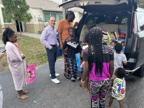 People gathered around an open minivan, loading supplies into the trunk in a neighborhood driveway.