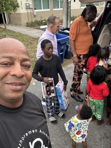 Group of people standing by a van and trash bins outside a house, with one person taking a selfie.