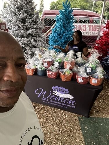 Man posing beside a Women’s Expo table with gift baskets and a decorated Christmas tree in the background