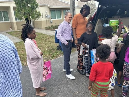 Neighbors gathered by an SUV, unloading items in front of apartment buildings.