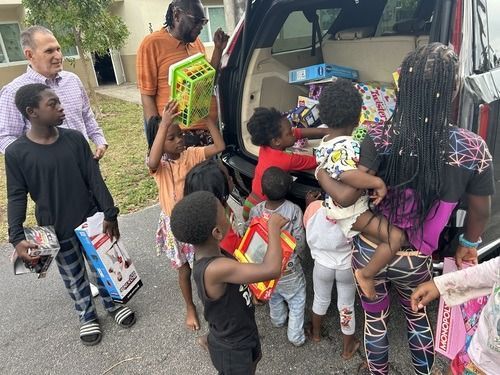 Children gather around an open vehicle, loading colorful gift boxes and toys in an outdoor setting