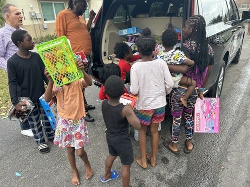 People gathered by a van, loading items and colorful packages on a wet street