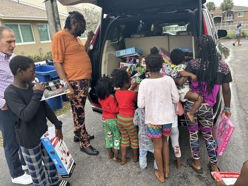 People gathering donated items from the open back of a van in a neighborhood driveway