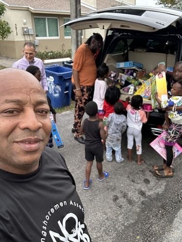 Man taking selfie while people gather around an open SUV loaded with donations on a residential street