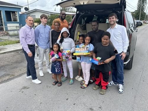 Group posing beside open van, holding donated toys and supplies, smiling on a street.