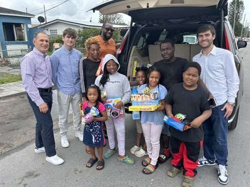 Group posing outdoors beside open van, holding food boxes and smiling.