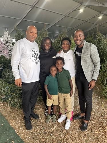 Five people posing together indoors, smiling in front of Christmas trees and a tent-like ceiling.