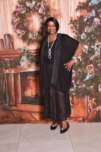 Woman in black dress posing in front of a floral painted backdrop.