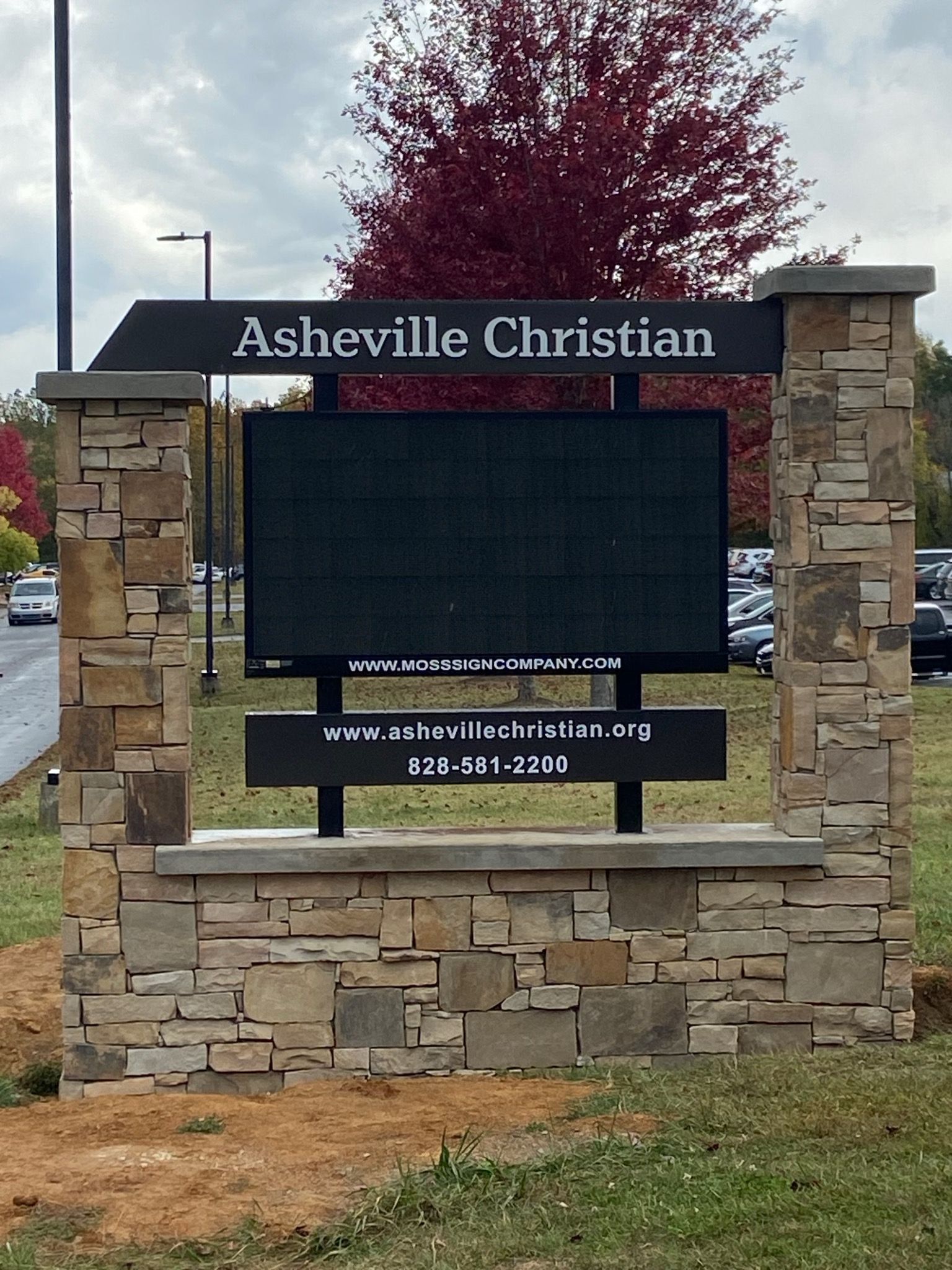 Asheville Christian school sign made of stone with a digital display board. The sign is located outdoors with fall foliage in the background.