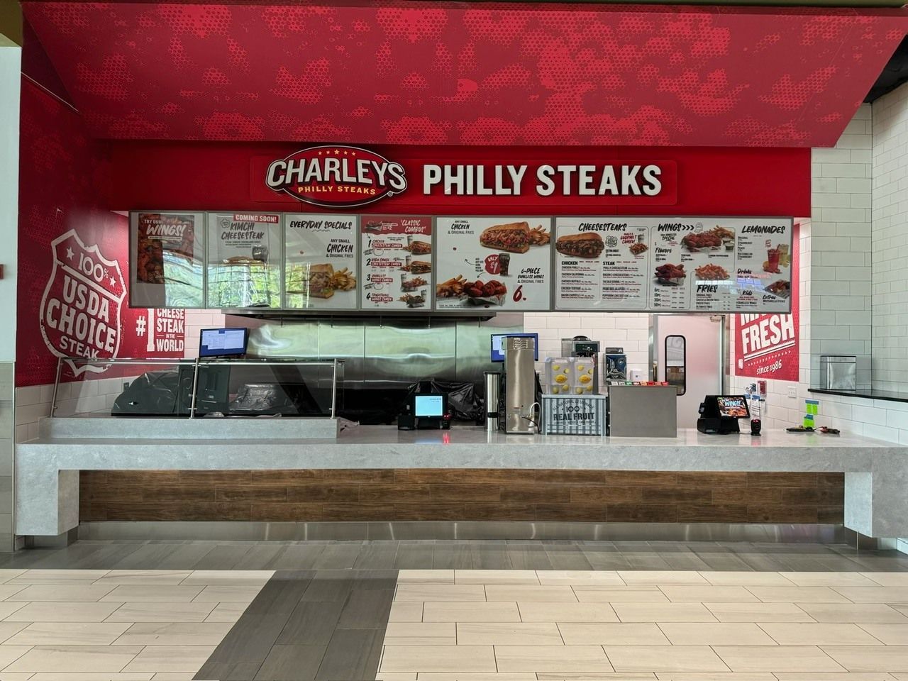 Charley's Philly Steaks counter at a food court. Red signage with menu boards. White countertop with equipment.