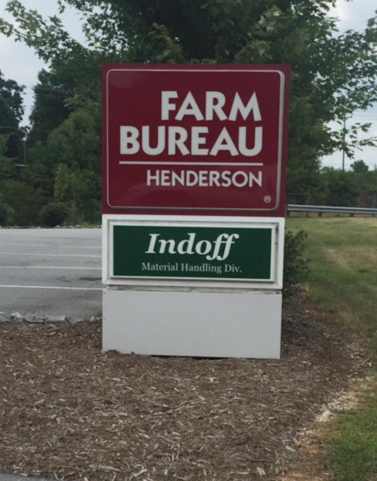 Sign for Henderson Farm Bureau and Indoff, a material handling division. Red and green panels atop a white base, outdoors.