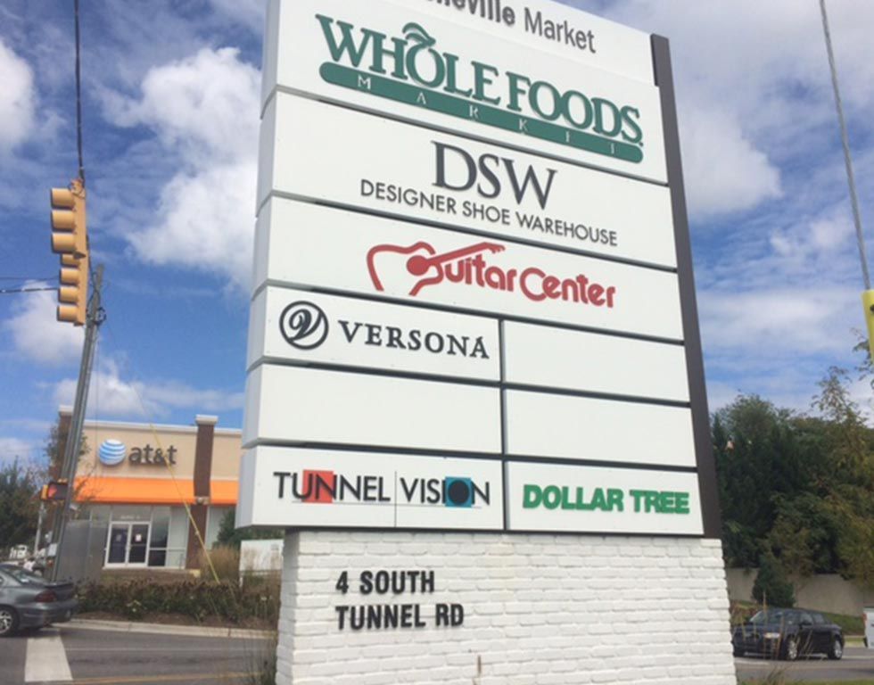 Signpost for a shopping center in Fayetteville, AR, including Whole Foods, DSW, Guitar Center, and other stores.