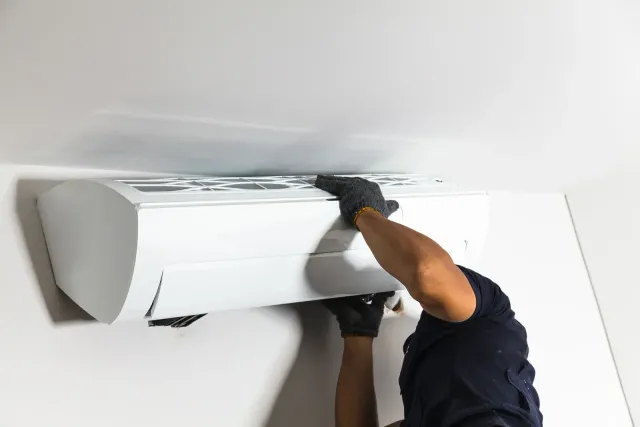 Man installing a white air conditioning unit on a light-colored wall.
