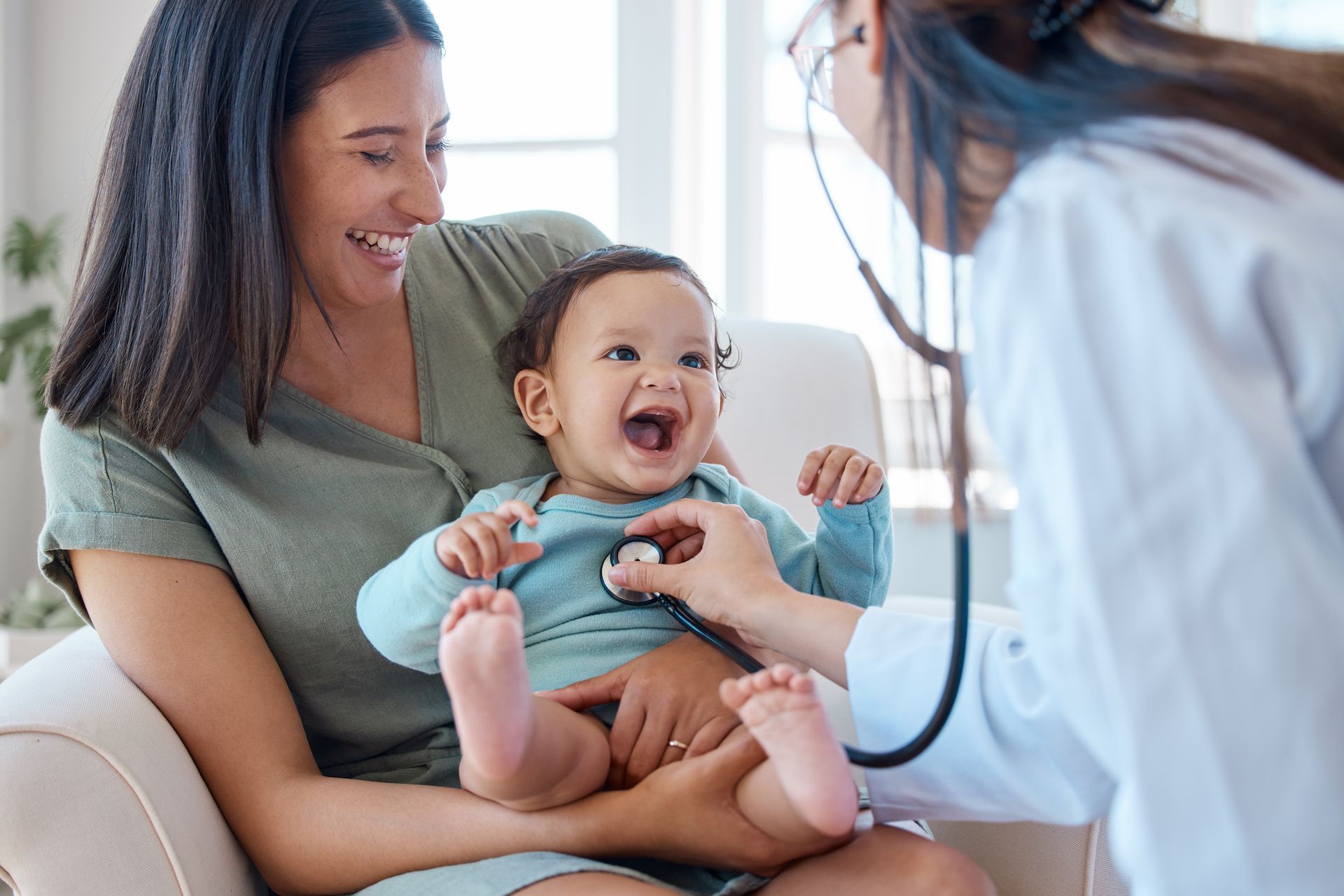 Mother holding baby getting checked by a doctor.