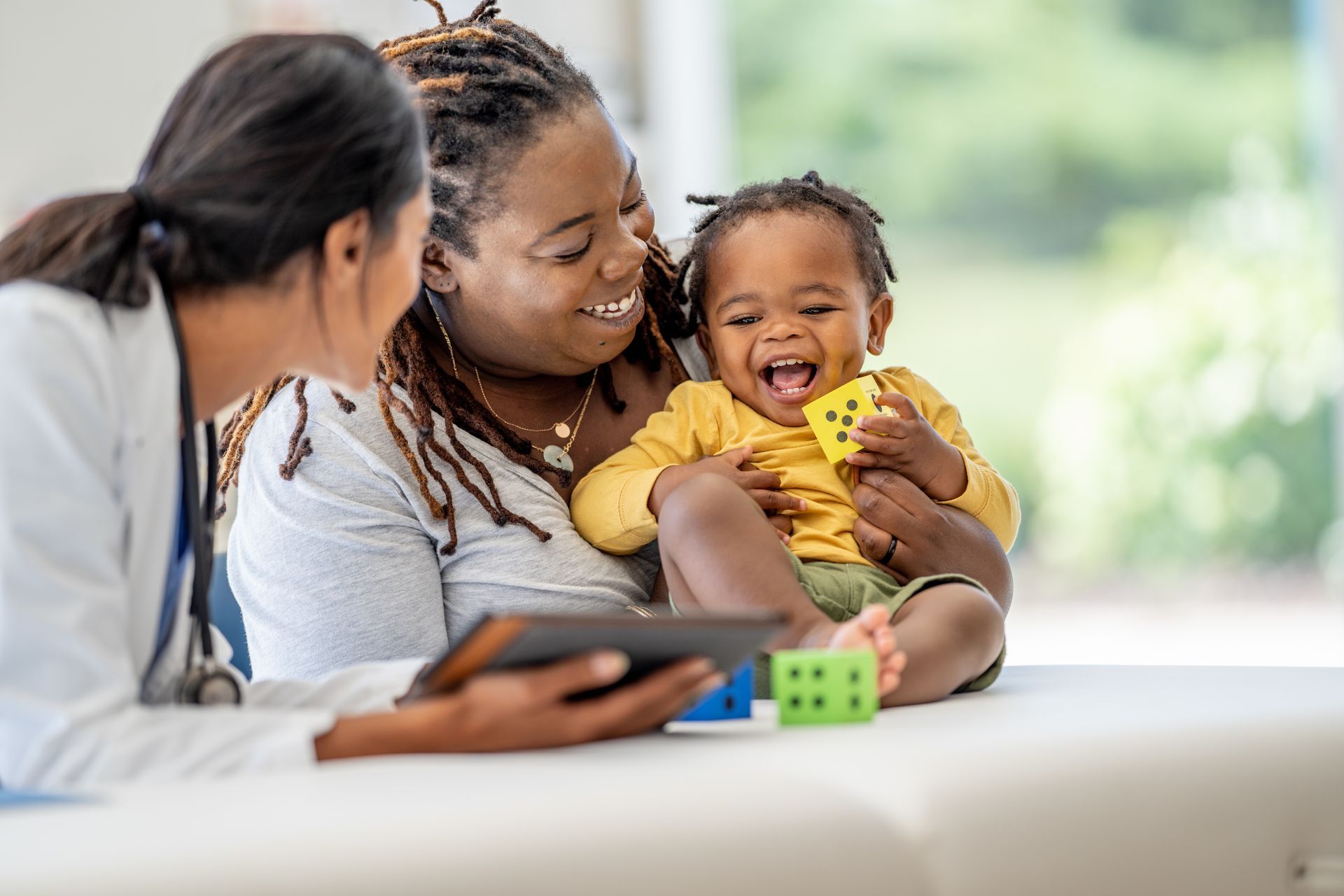 A woman is holding a baby while a doctor looks at a tablet.