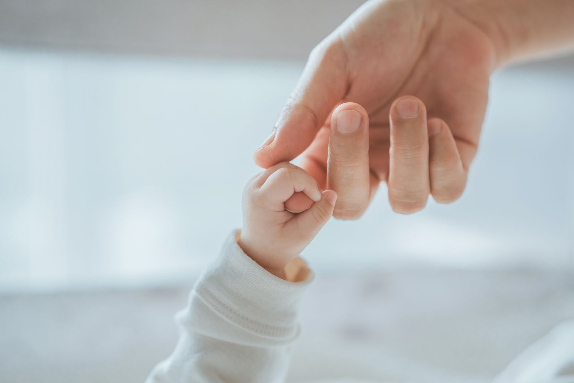 Adult hand holding a baby's hand.