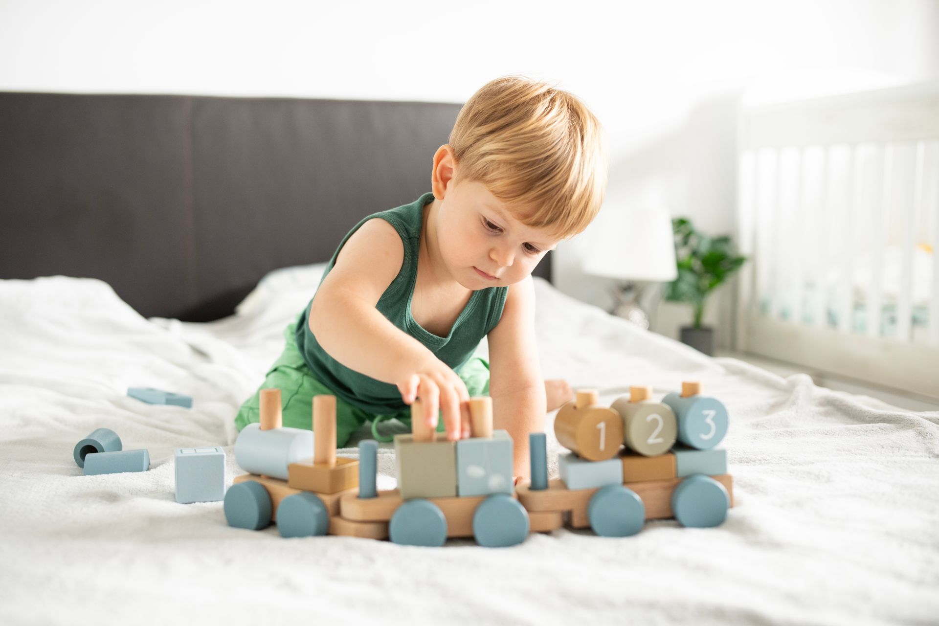 A young boy playing with wooden cars on a bed.