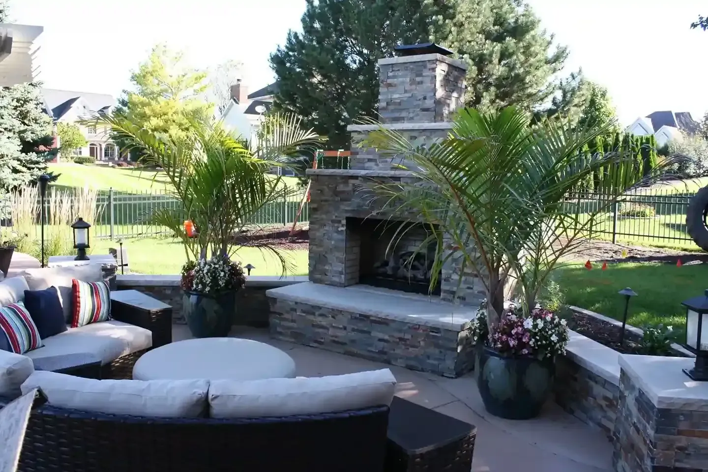 Outdoor patio with sectional seating and a stone fireplace in a landscaped backyard