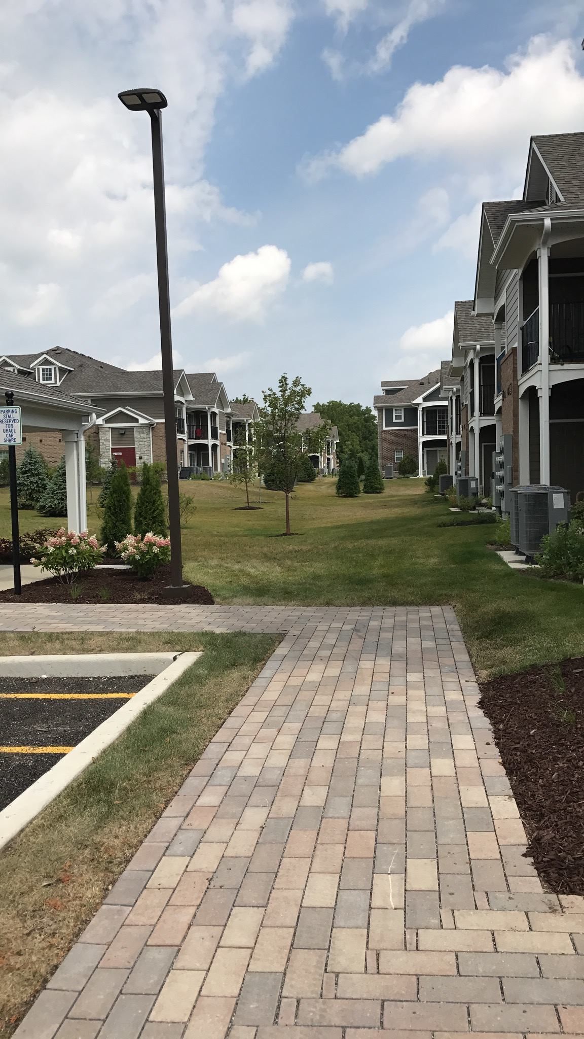 Brick sidewalk leading through a residential courtyard with townhouses, a lamppost, and grassy landscaping.