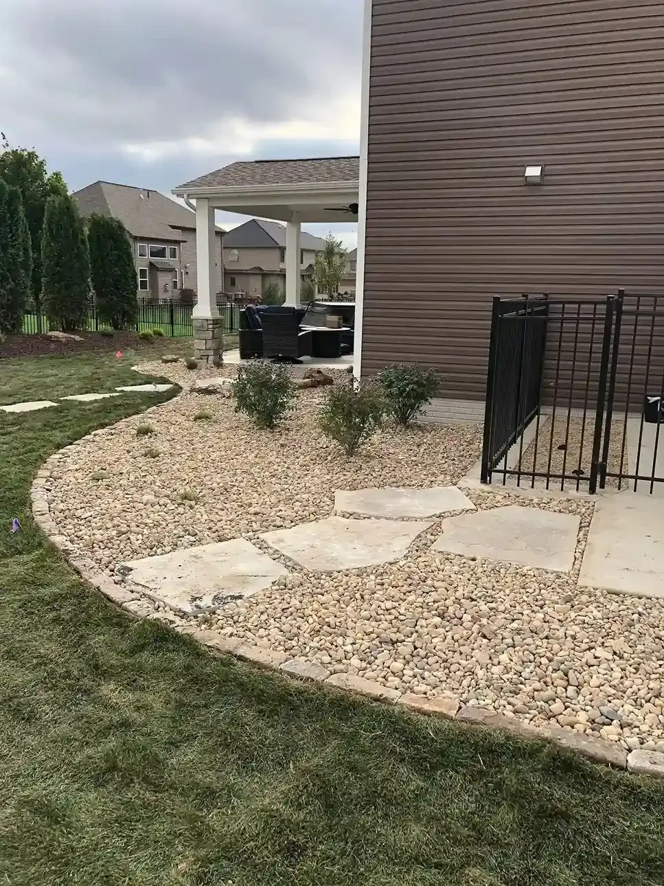 Backyard with gravel garden bed, stepping stones, lawn, and patio beside a house and pergola
