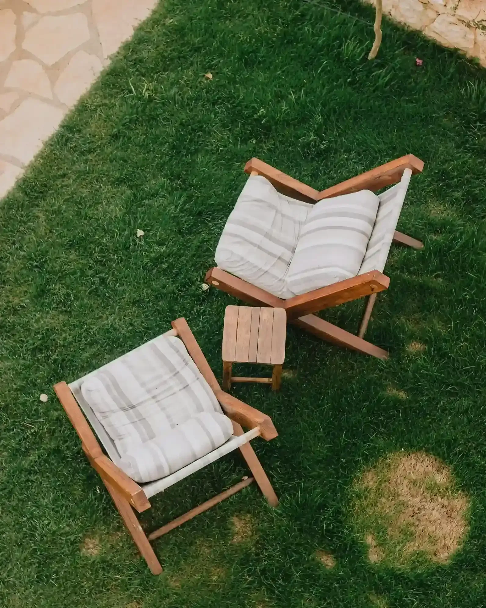 Two wooden lounge chairs with striped cushions and a small table on grass outdoors.