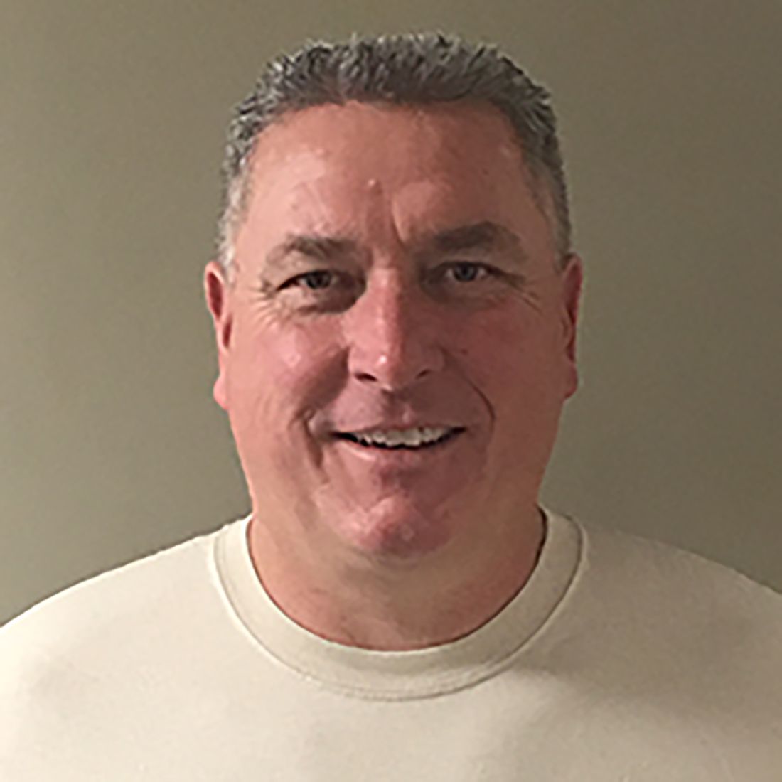 Smiling man in a cream shirt against a plain beige background