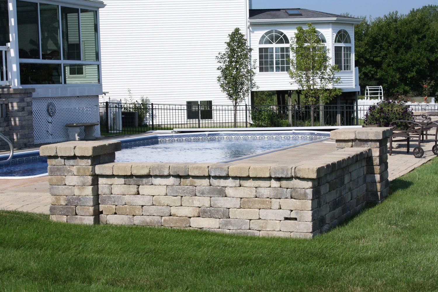 Stone-raised empty outdoor pool or planter beside a building with green lawn and patio furniture