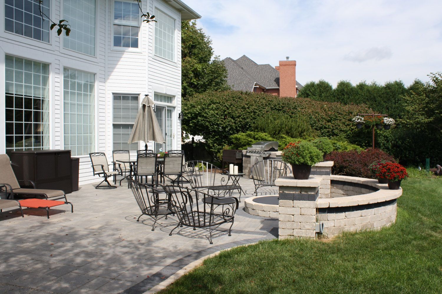 Patio with outdoor furniture beside a white house and stone fire pit in a landscaped backyard