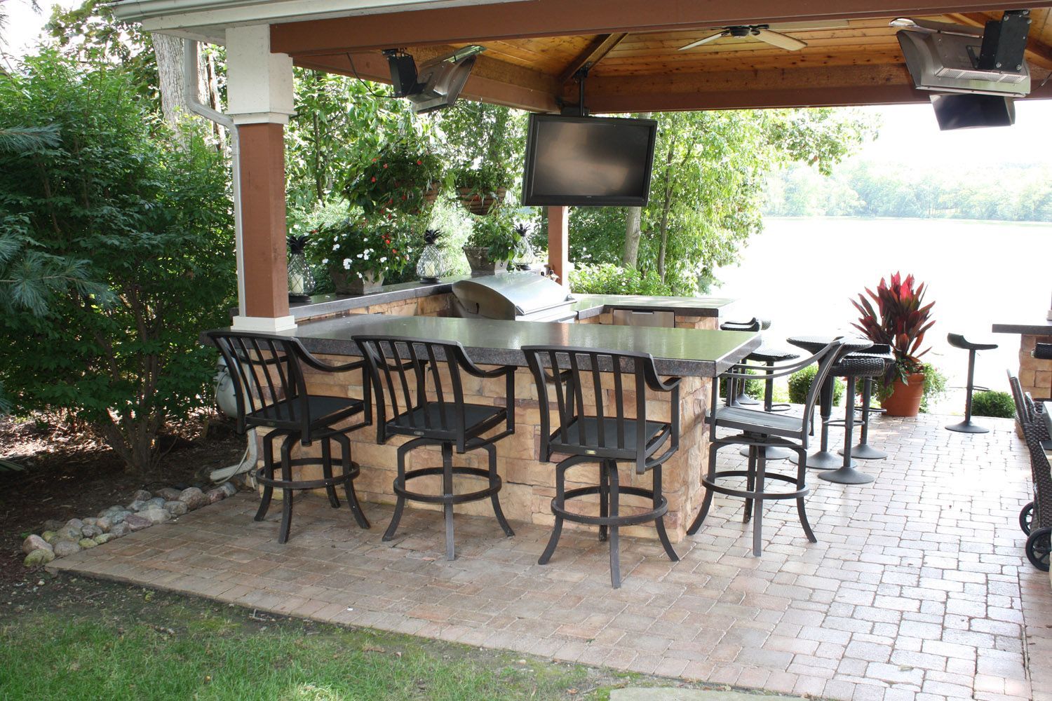 Covered outdoor patio with bar seating, tables, and a mounted TV surrounded by greenery