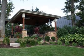 Landscaped garden with a stone-and-wood pavilion surrounded by trees and flowering shrubs