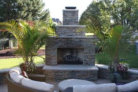 Stone outdoor fireplace in a landscaped backyard with curved seating and palm trees