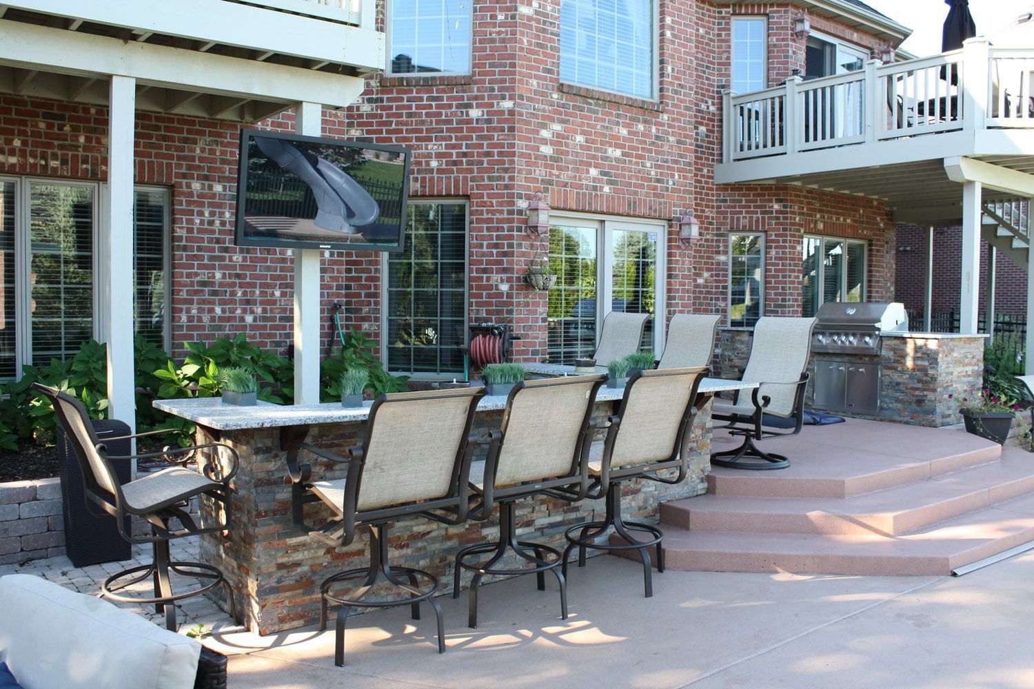 Brick patio with outdoor dining table, chairs, and a brick house with patio seating and balcony.