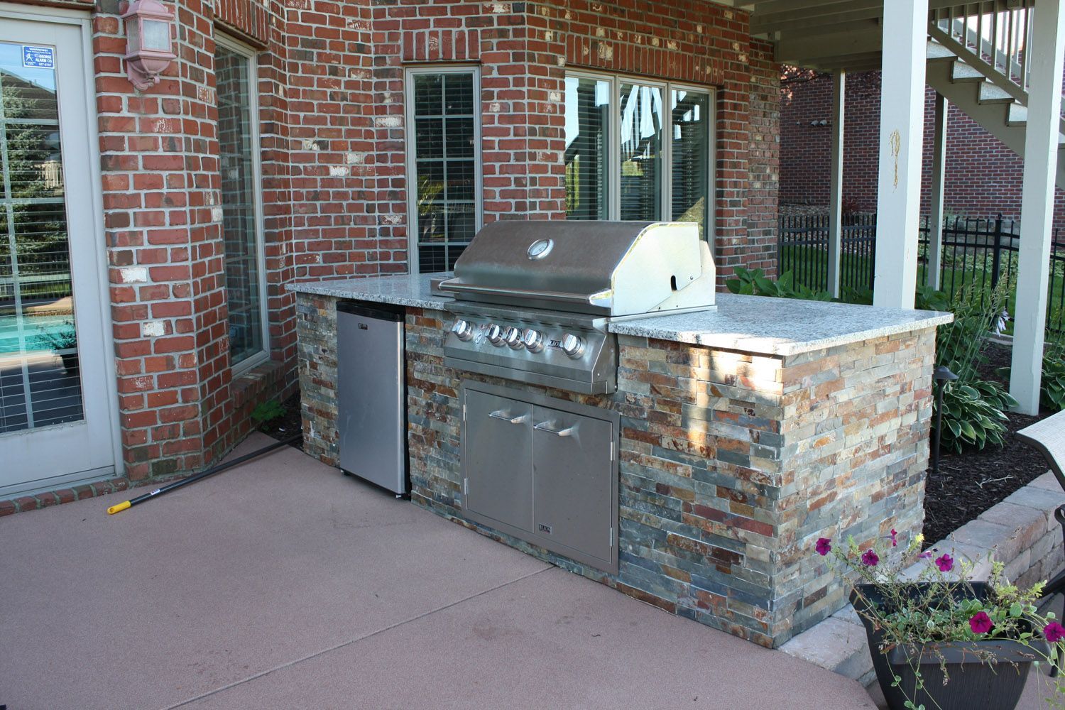 Outdoor built-in stainless steel grill beside a brick patio and stone counter