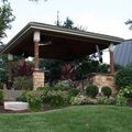 Landscaped garden with a stone pavilion and wooden roof, surrounded by shrubs and flowers