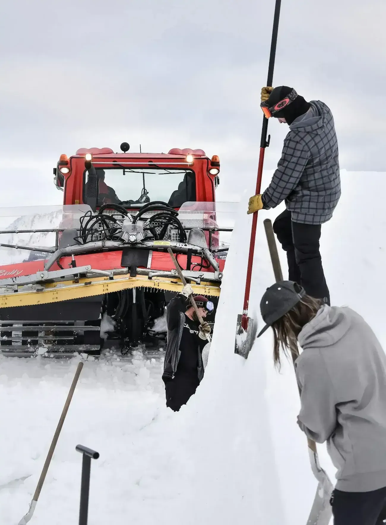 Tow truck winching a car out of deep snow while two workers guide it