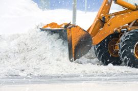Orange snowplow clearing a large pile of snow on a snowy road